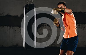 Concentrated young sportsman training thai boxing with punching bag