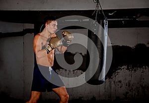 Concentrated young sportsman training thai boxing with punching bag