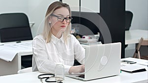 Concentrated young woman in glasses typing on the laptop at her office desk