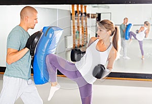 Concentrated young woman kicking boxing shield in gym