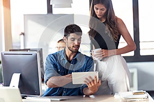 Concentrated young woman standing next to her man colleague pointing at something on digital tablet while working together in