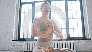 Concentrated young woman in stylish beige tracksuit does padma asana with namaste mudra meditating
