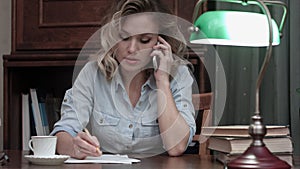 Concentrated young woman talking business on the phone and making notes at her desk