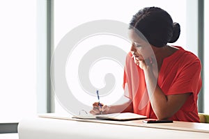Concentrating young African American female entrepreneur writing in her notebook