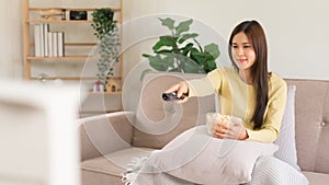 Concept of activity in home, Young woman holds remote control to changing channel and eats popcorn