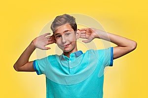 The concept of adolescence and emotions in adolescents. A teenage boy in a blue t-shirt, cheerfully pulling his ears with his