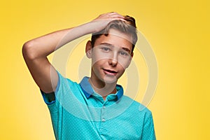 The concept of adolescence and emotions in adolescents. A teenage boy in a blue t-shirt, smiling uncertainly, scratches