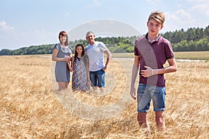 Concept of adopted kid, boy standing on foreground with adoptive family on background, stepson with dad, mom and preteen sister