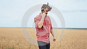 Concept of agriculture young farmer man speaking on phone and walking through the young wheat field he enjoying the time