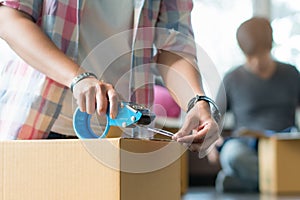 Concept young couple moving house. Close-up hand of woman use tape sealing cardboard box