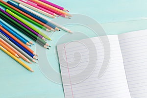 Concept back to school.School accessories, colored pencils, pen with empty notebook on blue wooden background