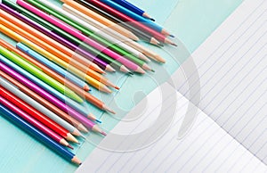 Concept back to school.School accessories, colored pencils, pen with empty notebook on blue wooden background