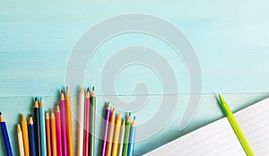 Concept back to school.School accessories, colored pencils, pen with empty notebook on blue wooden background