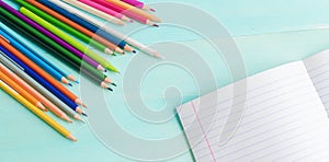 Concept back to school.School accessories, colored pencils, pen with empty notebook on blue wooden background