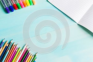 Concept back to school.School accessories, colored pencils, pen with empty notebook on blue wooden background