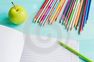 Concept back to school.School accessories, colored pencils, pen with empty notebook on blue wooden background