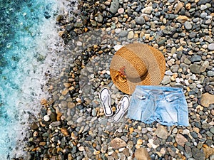 The concept of beach holidays and tourism. Straw hat, slates and shorts on a pebble beach by the sea. Summer holidays