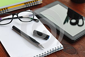 The concept: the beginning of work. Pen, open notebook, tablet computer and glasses on office desk.