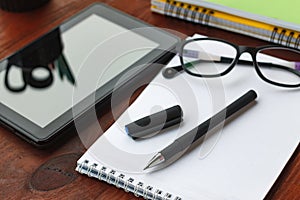 The concept: the beginning of work. Pen, open notebook, tablet computer and glasses on office desk.