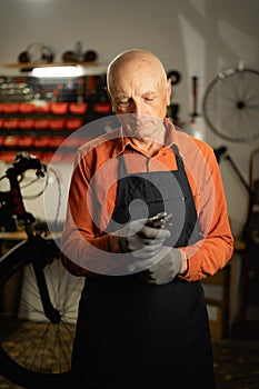 Concept of bicycle maintenance. Portrait of elderly cycling repairman holding wrench standing near bicycle in repair