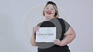 Concept body positivity - a chubby smiling woman dancing and holds a sign with the inscription I LOVE MYSELF