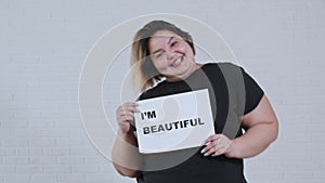 Concept body positivity - an overweight smiling woman dancing and holds a sign with the inscription I'M BEAUTIFUL