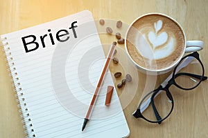 Concept Brief on notebook with glasses, pencil and coffee cup on wooden table