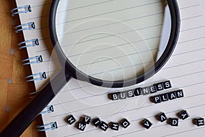 concept of Business Plan word on wooden cubes with magnifying glass, books in background