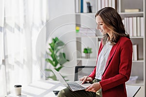 Concept of business working, Businesswoman wearing red suite sitting on her desk while using computer laptop for checking business