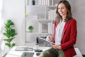 Concept of business working, Businesswoman wearing red suite sitting while writing and checking business analytic document report