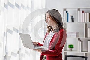 Concept of business working, Businesswoman wearing red suite standing while using computer laptop for checking business analytic