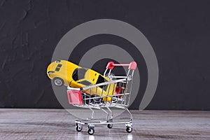 Concept of buying a new car. Toy car in shopping basket on wooden background