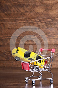 Concept of buying a new car. Toy car in shopping basket on wooden background