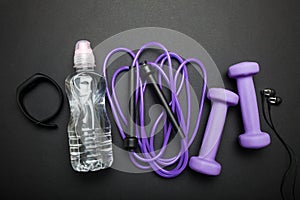 The concept of cardio training. Weights, jamp rope, headphones, fitness bracelet and water. Black background photo