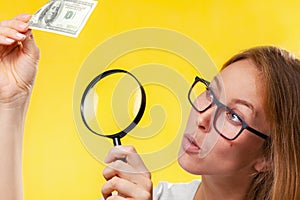 The concept of checking counterfeit money. A blond woman with interest in looking at a dollar bill through a magnifying glass, photo