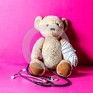 Concept of child playing doctor with teddy bear, pink background