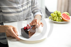 Concept of choice between healthy and junk food. Woman eating cake at white table, closeup