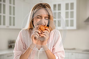 Concept of choice between healthy and junk food. Woman eating croissant in kitchen