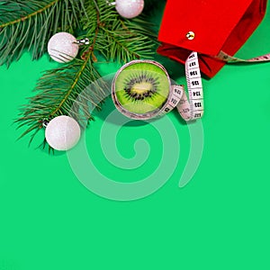 Concept Christmas holidays diet and healhty lifestyle - kiwi and tape measure with red gift bag on trendy green blue