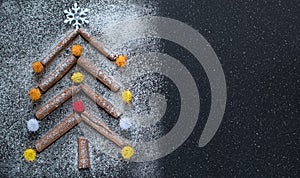 Concept of Christmas and New Year - Christmas tree made of cinnamon sticks on a black background with flour, decorated with a