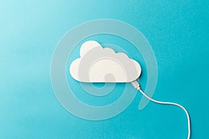 The concept of cloud technologies, cloud storage. A white cable is connected to a cloud on a blue background. Top view. Flat lay