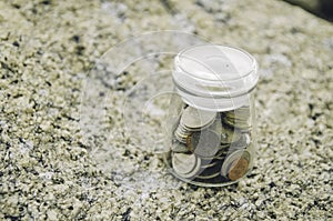 Concept of coin in glass jar on the rock.
