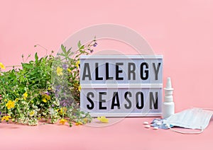 The concept combating preventing seasonal allergies. Fresh flowers medical mask pills drops medicine pink background.