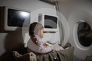 Concept of comfortable flight with infant. little cute toddler sitting in a bassinet and reading a book