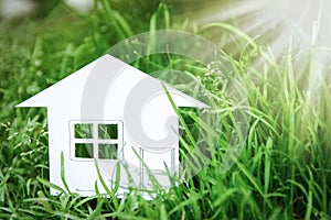 The concept or conceptual house white paper in his hand in a green summer grass on a background, a symbol for the construction,