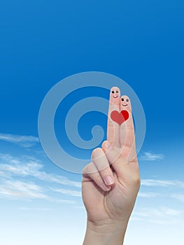 Human or female hands with two fingers painted with a red heart and smiley faces over cloud blue sky