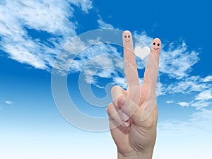 Human or female hands with two fingers painted with a white heart and smiley faces over cloud blue sky