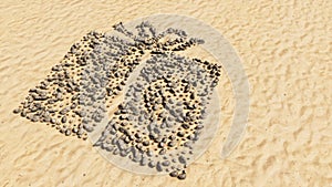 Stones on beach sand handmade symbol shape, golden sandy background, present wrapped box sign