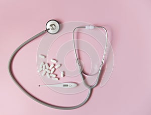 Concept control your health. Stethoscope thermometer and pills with place for text top view on a pink background