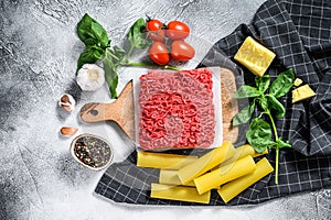 The concept of cooking cannelloni pasta with ground beef. ingredients Basil, cherry tomatoes, Parmesan, garlic. Gray background.